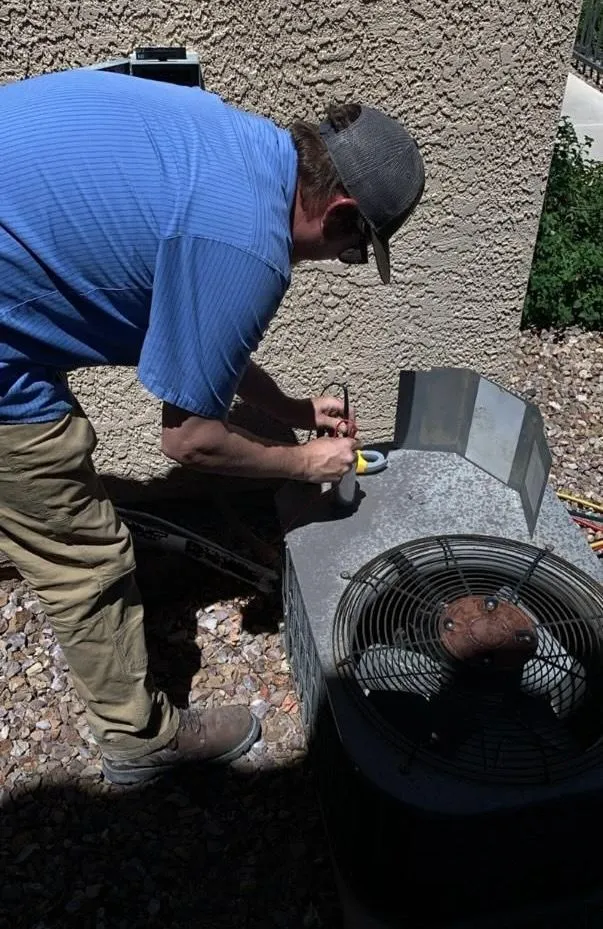 We Care Air technician servicing an outdoor AC condenser at a Boulder City home